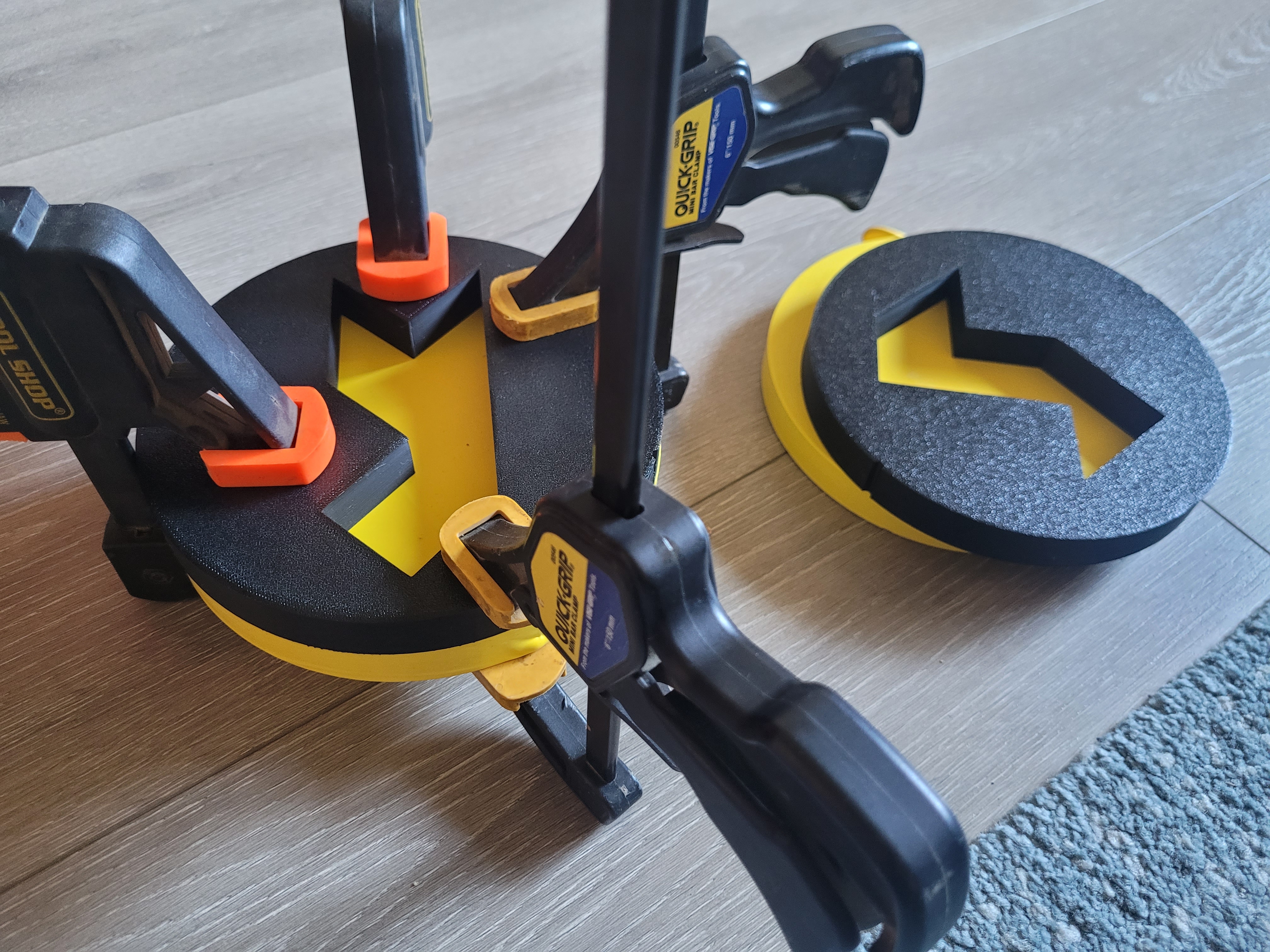 Some 3D-printed plastic discs, each with a big polygonal hole. Two of them are clamped together with wood clamps, with a piece of a yellow balloon sandwiched between.